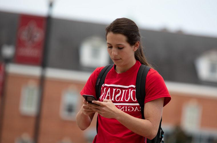 UL Lafayette student walking through the Quad while looking at her phone