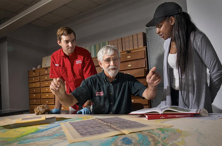 A University of Louisiana at Lafayette research professor looks over maps of the 海岸 line with two students looking over his shoulders