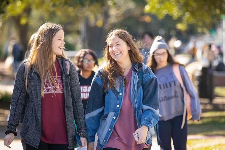 Two University of Louisiana at Lafayette female students smile and laugh while walking on campus